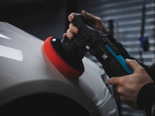 A machine polisher working across a front fender